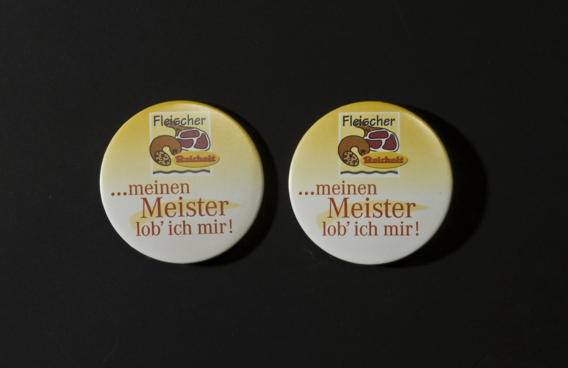 Zwei Buttons der Firma "Reichelt" - "Fleischer  meinen Meister lob ich mir" (Stiftung Domäne Dahlem - Landgut und Museum, Weiternutzung nur mit Genehmigung des Museums CC BY-NC-SA)