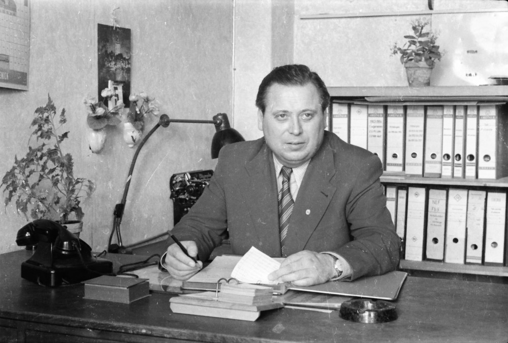 Mann mit Parteiabzeichen am Büroschreibtisch. ; Foto, Oktober 1955 (www.industriesalon.de CC BY-NC-SA)