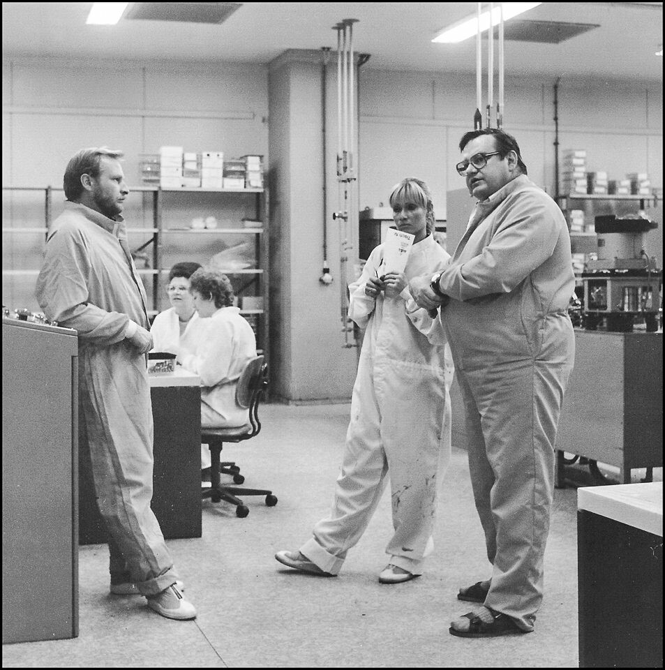 Zwei Männer und eine Frau in Schutzkleidung stehen bei einer Besprechung in der Abteilung Mikrochip Produktion des WF, SW-Foto © Kurt Schwarz, 1980er Jah (Kurt Schwarz CC BY-NC-SA)