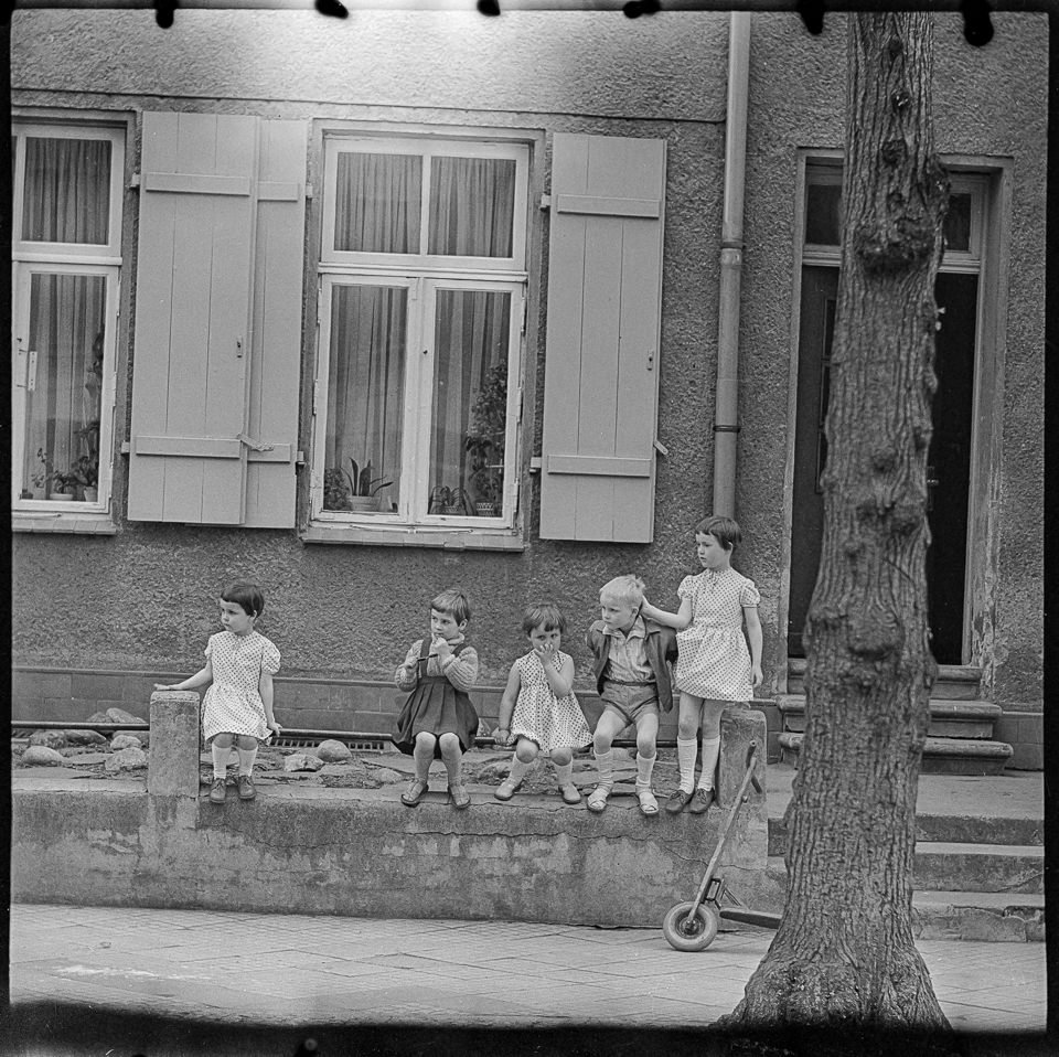 Fünf Kinder sitzen vor einem Wohnhaus, 1960er Jahre. SW-Foto © Kurt Schwarz. (Kurt Schwarz CC BY-NC-SA)