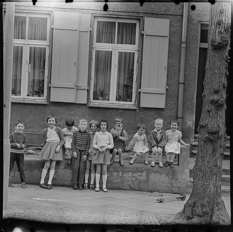 Zehn Kinder sitzen und stehen lachend vor einem Wohnhaus, 1960er Jahre. SW-Foto © Kurt Schwarz. (Kurt Schwarz CC BY-NC-SA)