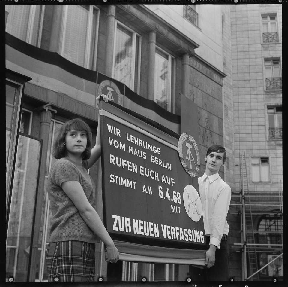 Volksentscheid zur neuen Verfassung der DDR am 6. April 1968, Bild 2: Junge Frau und junger Mann halten ein Schild, das für die Annahme der neuen Verfassun (Kurt Schwarz CC BY-NC-SA)