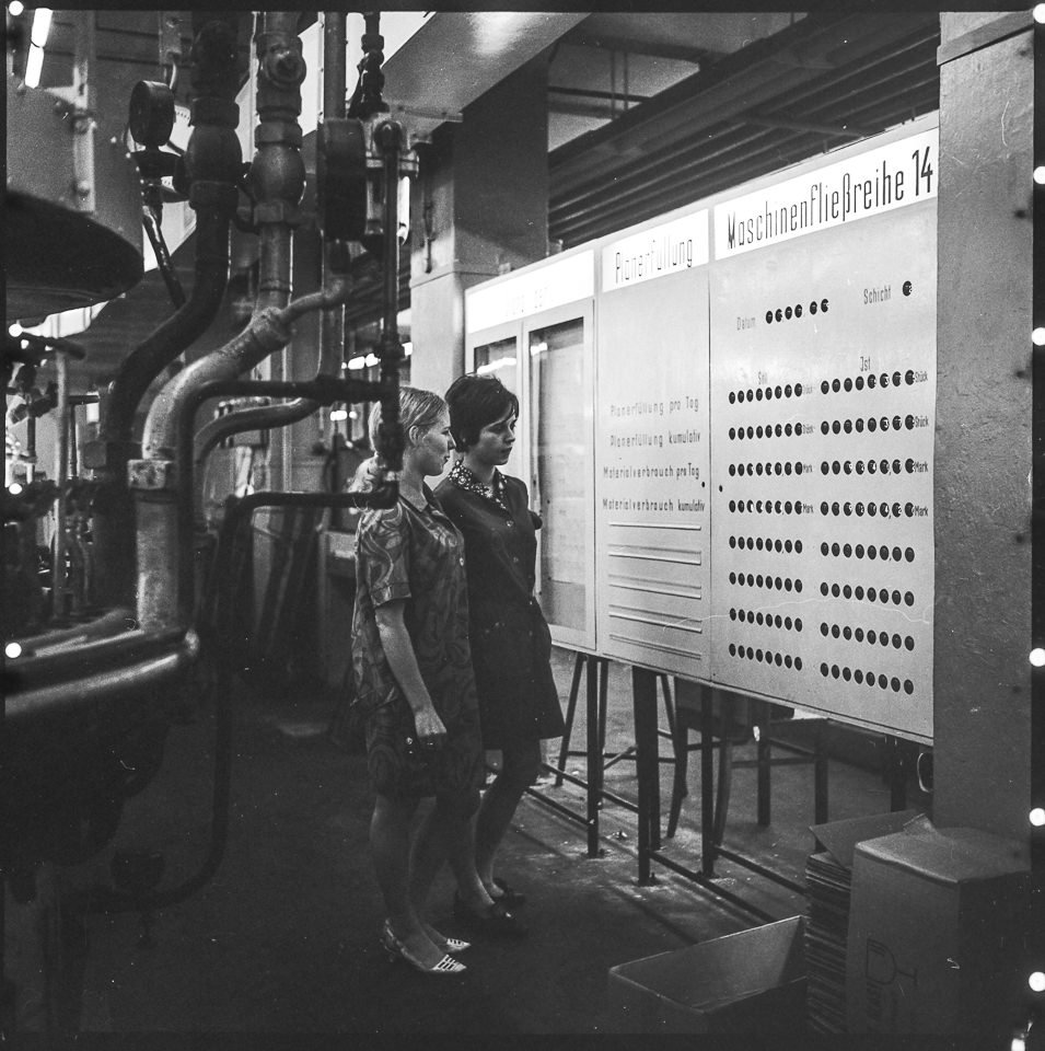 VEB Narva Kombinat, Bild 5: Zwei Frauen betrachten eine Informationstafel mit Ergebnissen zur Planerfüllung. SW-Foto, Oktober 1969 © Kurt Schwarz. (Kurt Schwarz CC BY-NC-SA)