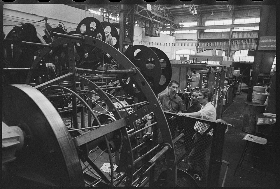 Kabelwerk Oberspree (KWO), Bild 3: Drei Männer der Brigade "DSF" in einer Fabrikhalle vor einer großen Kabelwickelmaschine. SW-Foto, September 1970 © Kurt (Kurt Schwarz CC BY-NC-SA)