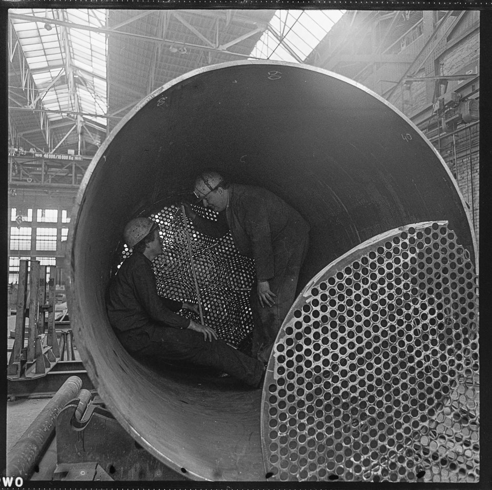 Zwei Männer mit Helm, die sich in in einem Großrohrstück befinden, im Gespräch, Szene in einer Fabrikhalle von VEB Bergmann-Borsig. SW-Foto, März 1968 © Ku (Kurt Schwarz CC BY-NC-SA)