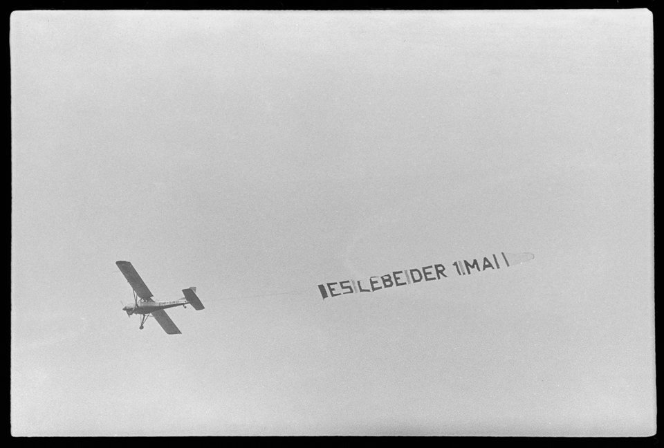 1. Mai Demonstration, Bild 3: Propellermaschine am Himmel zieht Spruchband: "Es lebe der 1. Mai". SW-Foto, Anfang der 1960er Jahre © Kurt Schwarz. (Kurt Schwarz CC BY-NC-SA)