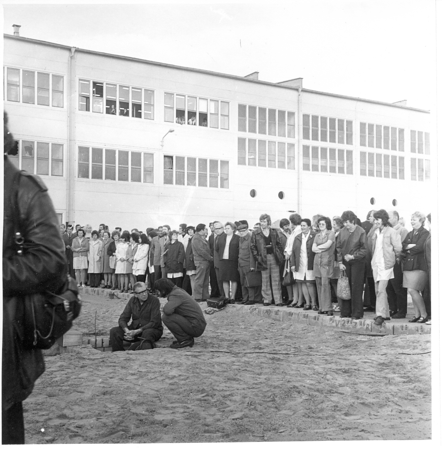 zwei Männer an Grube mit Kassette, im Hintergrund Menschenmenge, vorne links teileweise Mann in Lederjacke sichtbar (Industriesalon Schöneweide CC BY-SA)