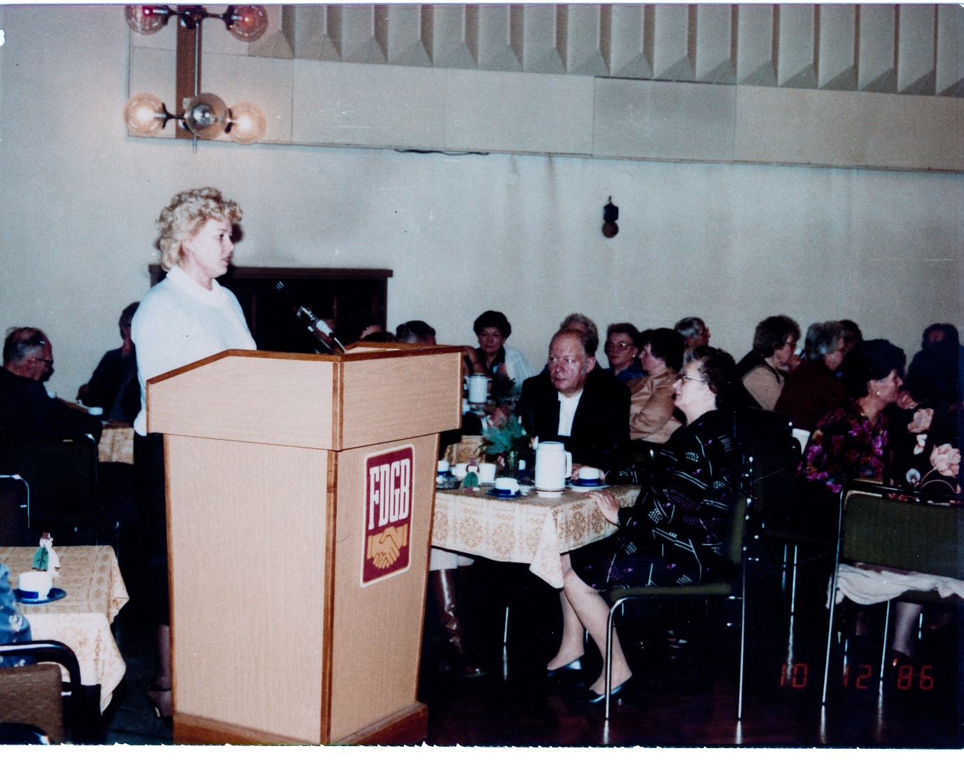 im Kulturhaus hält eine Frau hinterm Rednerpult eine Rede, Rednerpult mit Emblem des FDGB, im Hintergrund Tische mit weiteren Personen (Industriesalon Schöneweide CC BY-NC-SA)
