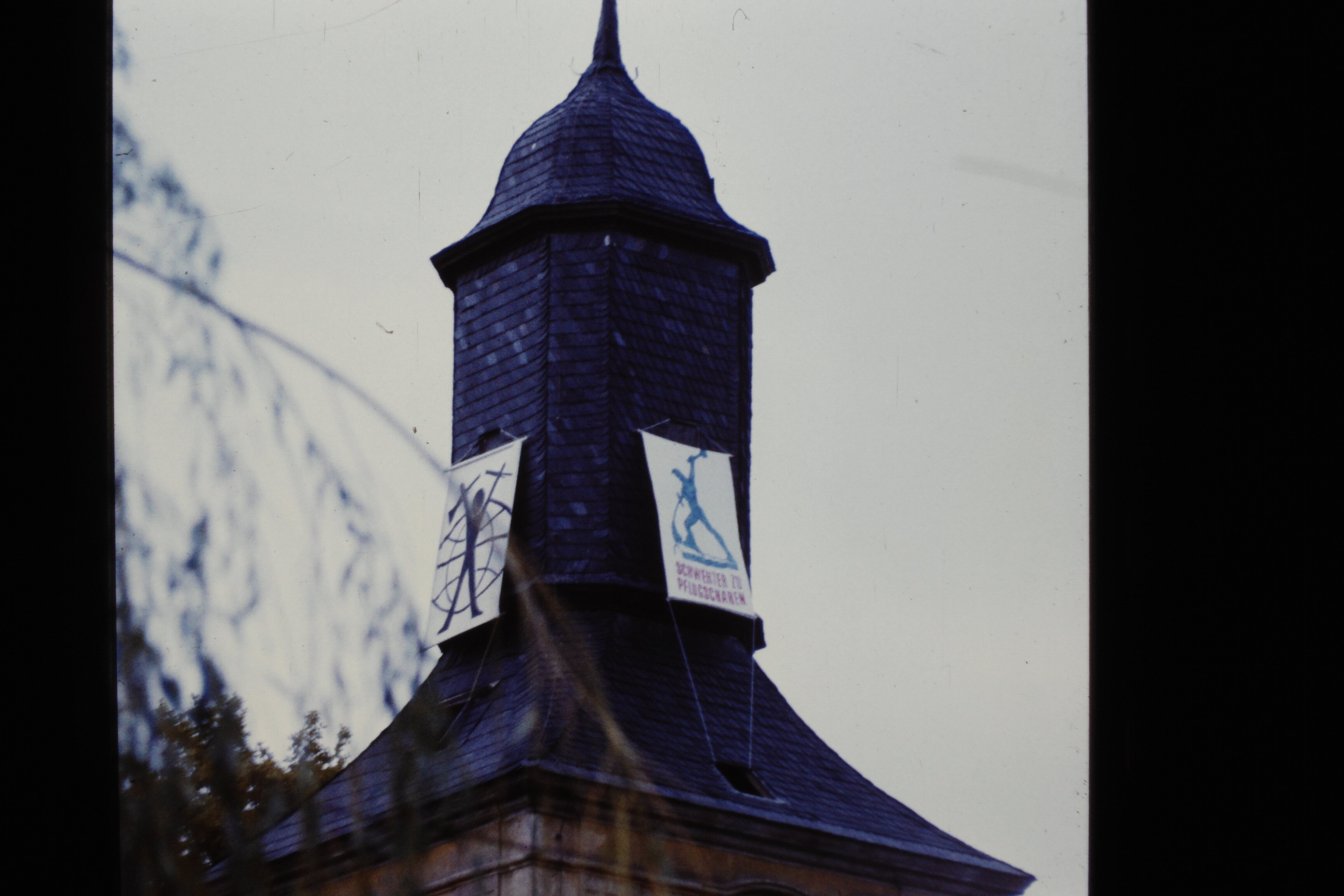Kirchturm der Köritzer Gemeinde in Neustadt (Dosse): Transparente mit aufgemaltem "Schwerter zu Pflugscharen" und "Mann vor Weltkugel" (DDR Geschichtsmuseum im Dokumentationszentrum Perleberg CC BY-SA)