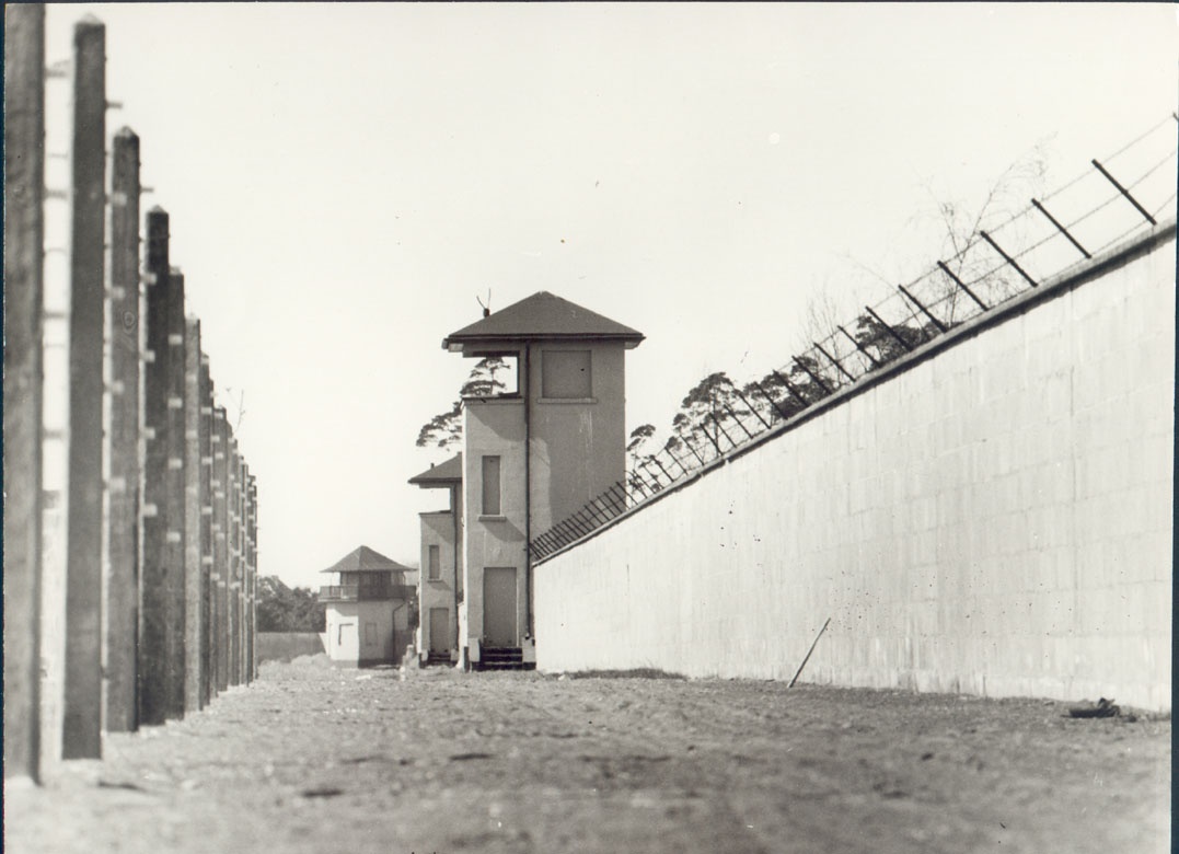 Wachturm an der Lagermauer, davor Stacheldrahtzaun (1961) (Gedenkstätte und Museum Sachsenhausen CC BY-NC-SA)