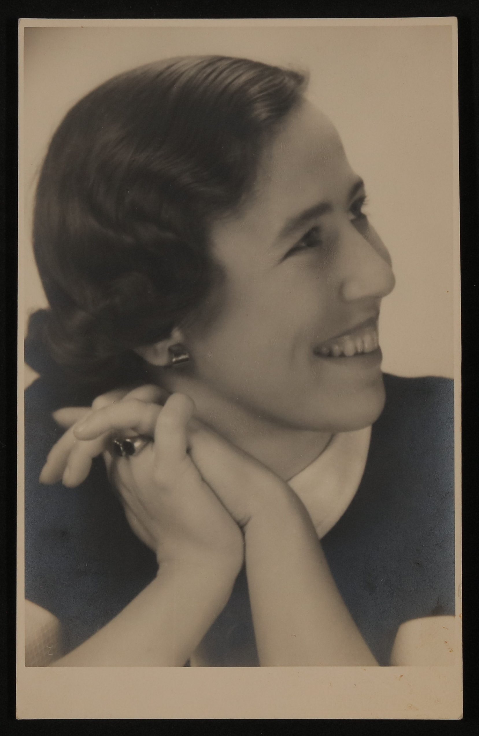Portrait einer unbekannten lachenden jungen Frau im Profil, mit vor dem Hals verschränkten Händen (Vera Graaf CC BY-NC-SA)