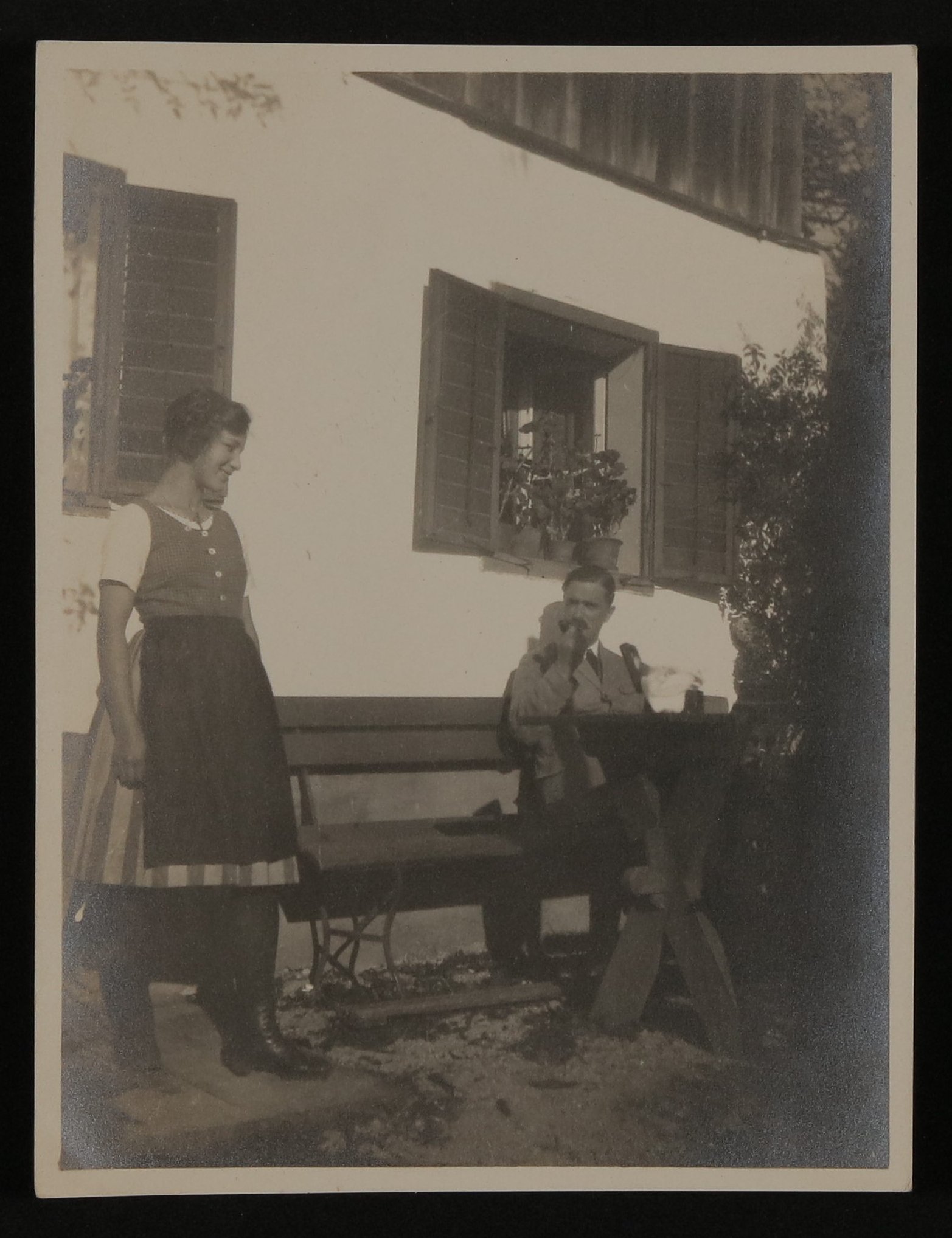 Carl Jacob Burckhardt sitzt rauchend vor einem Haus, daneben steht eine junge Frau (Vera Graaf CC BY-NC-SA)