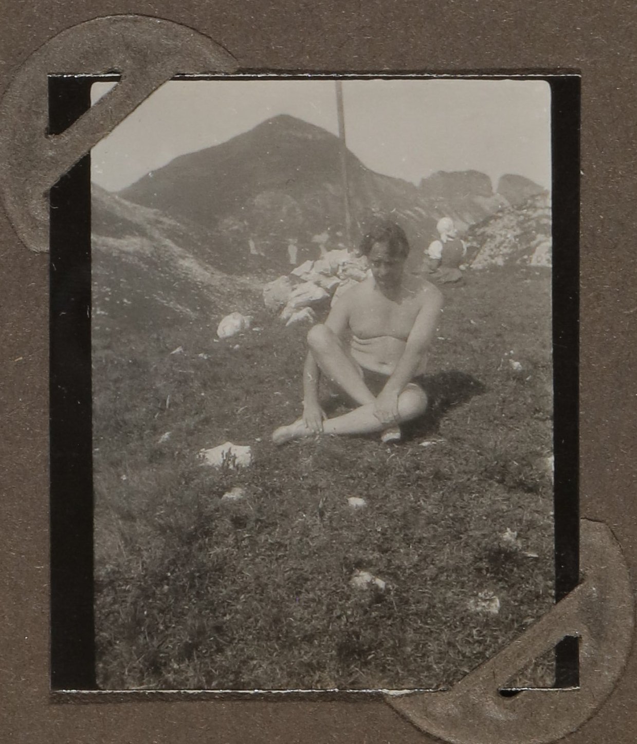 Heinrich Zimmer in Badehose auf einer Wiese vor Bergen sitzend (Vera Graaf CC BY-NC-SA)