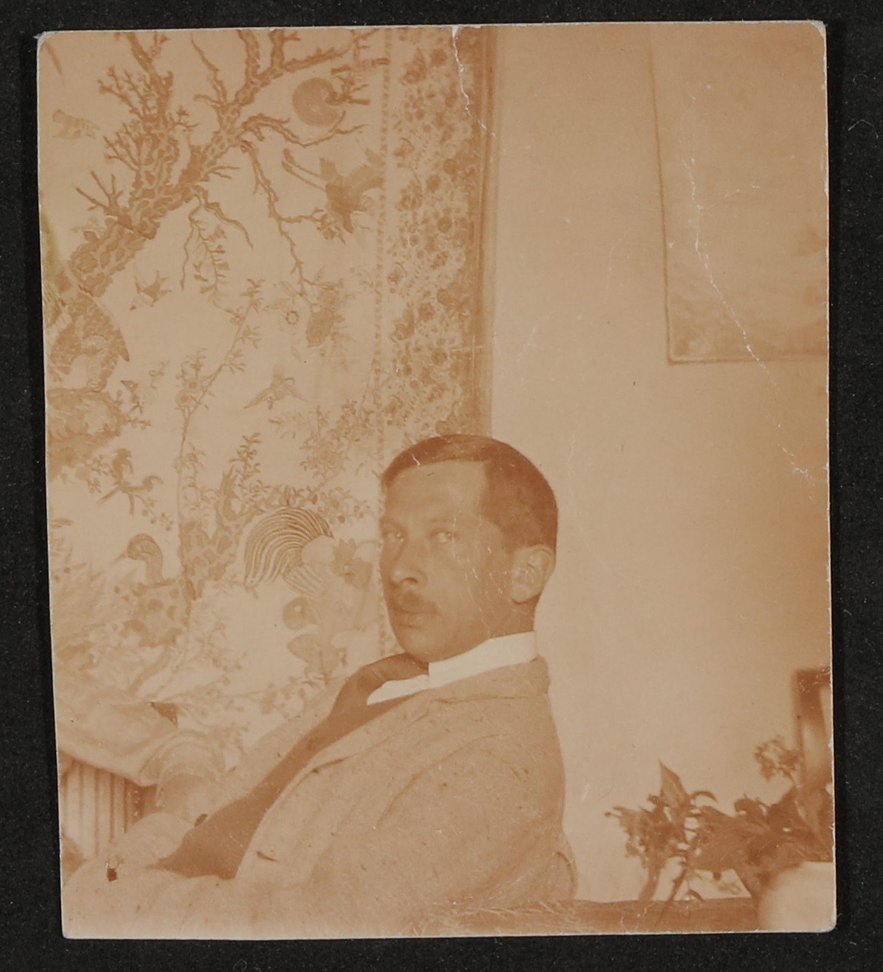 Rudolf Borchardt sitzt nach links gewendet, Blick über die Schulter in die Kamera vor einem chinesischen Wandteppich (Freies Deutsches Hochstift / Frankfurter Goethe-Museum CC BY-NC-SA)