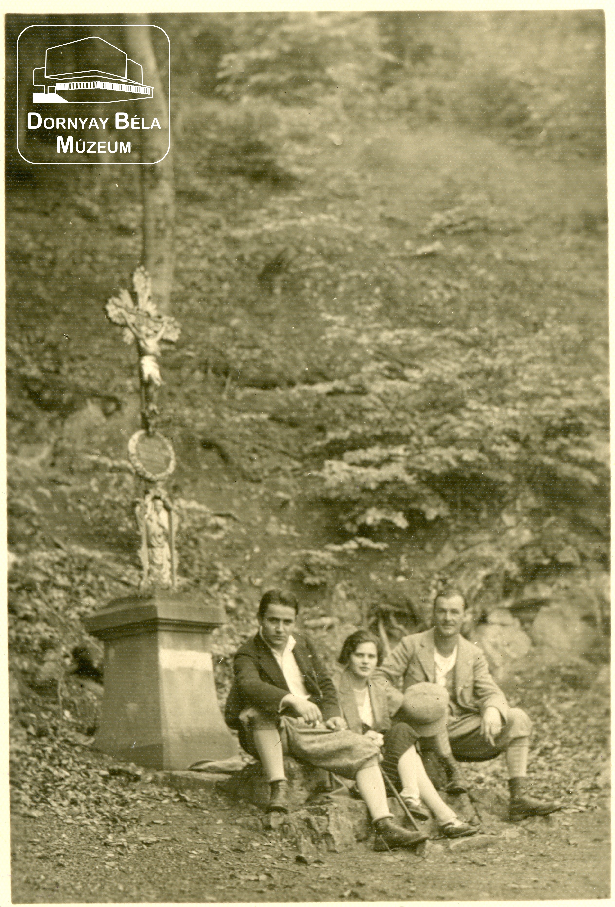 Túrázók egy útmenti kereszt előtt ülnek. Dr. Dornyay Béla gyűjteményéből. (Dornyay Béla Múzeum, Salgótarján CC BY-NC-SA)
