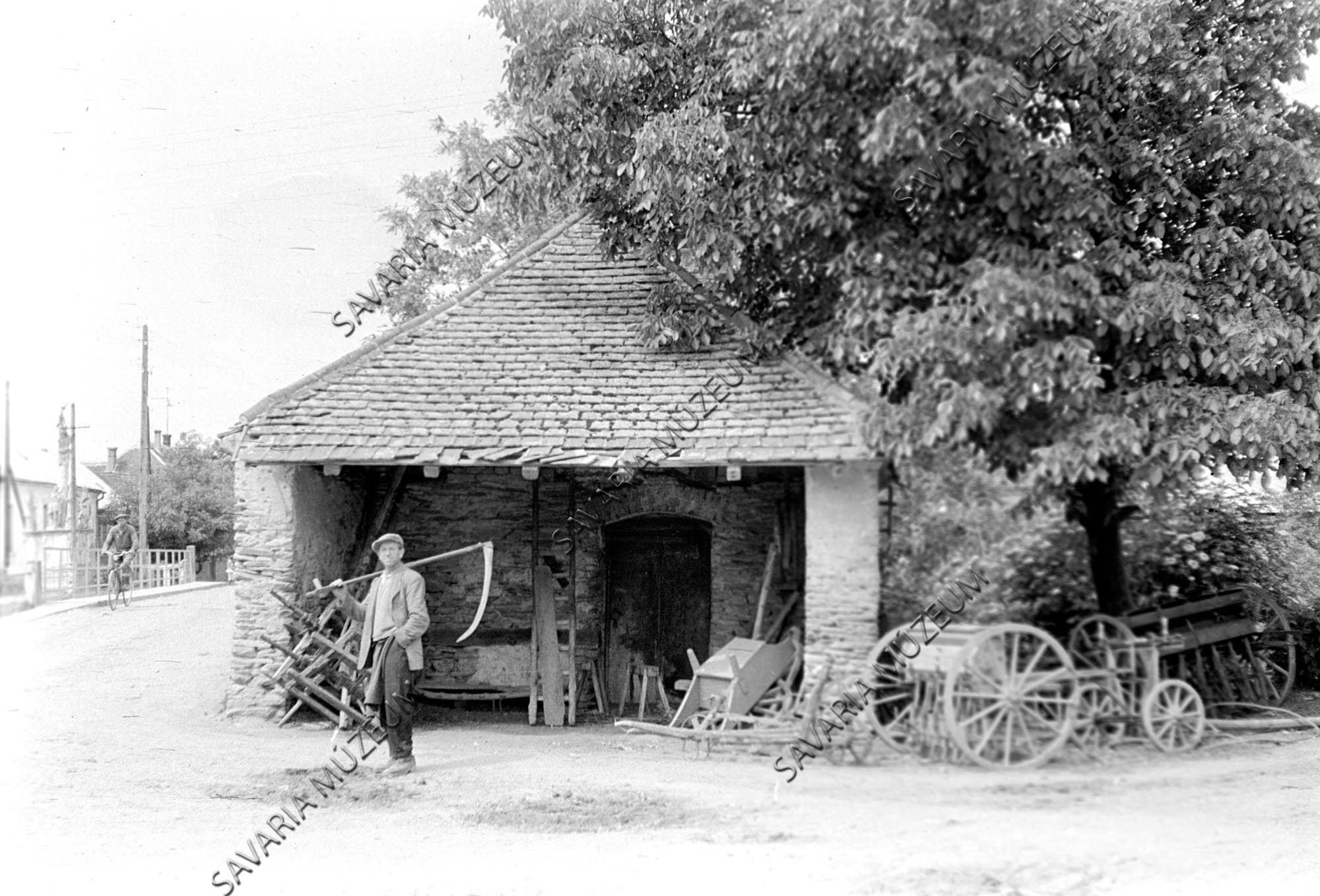Kovácsműhely, talicska, vetőgép, férfi kaszával (Savaria Megyei Hatókörű Városi Múzeum, Szombathely CC BY-NC-SA)