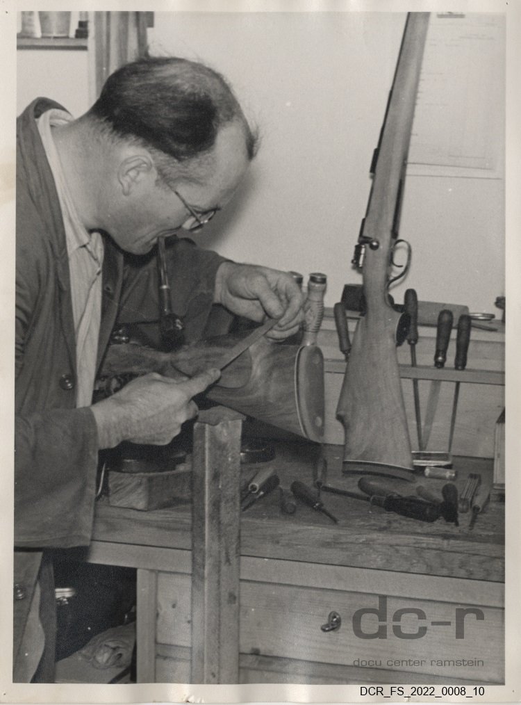 Schwarzweißfoto, Portraitaufnahme von Josef Fuchs beim Feilen an einem Gewehrkolben ("dc-r" docu center ramstein RR-F)