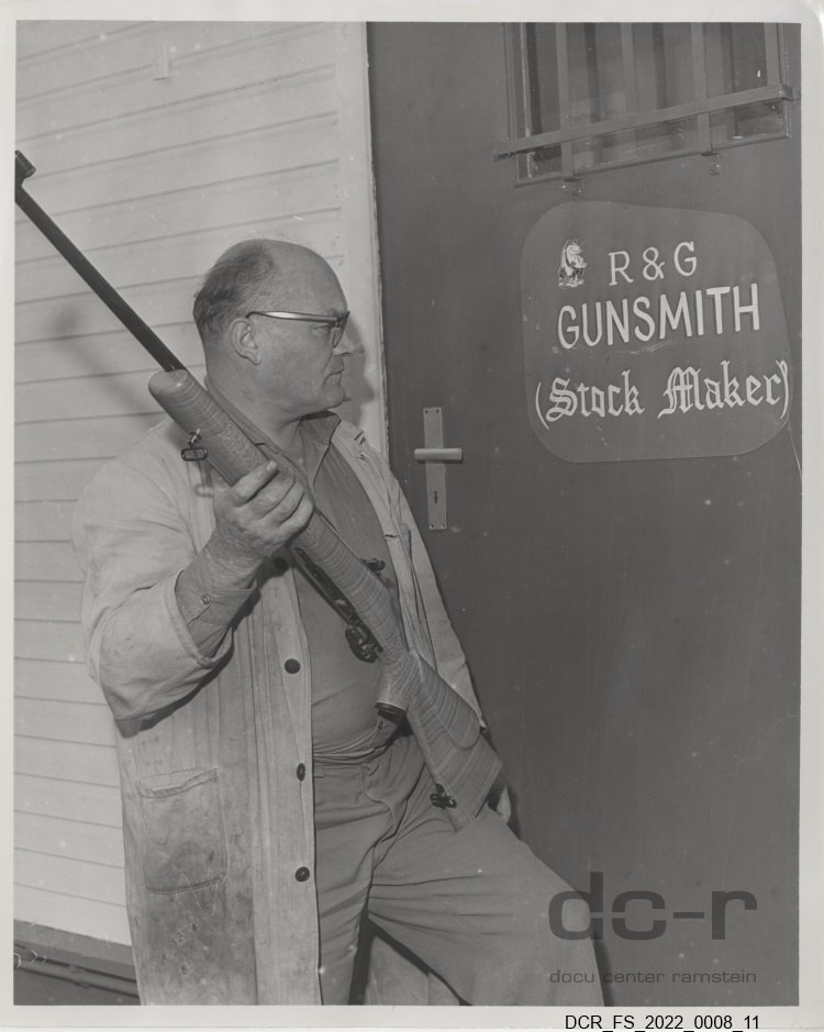 Schwarzweißfoto, Portraitaufnahme von Josef Fuchs mit einem Gewehr vor seiner Werkstatt ("dc-r" docu center ramstein RR-F)