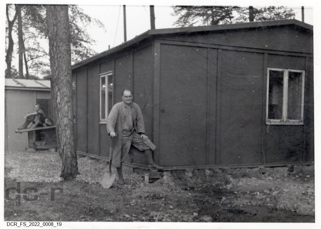 Schwarzweißfoto, Portraitaufnahme von Josef Fuchs mit einem Spaten vor seiner Werkstatt ("dc-r" docu center ramstein RR-F)
