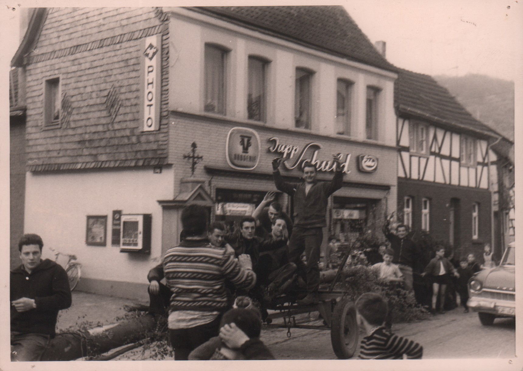 Junggesellen mit dem Maibaum vor dem Lebensmittelgeschäft Jupp Schuld auf dem Weg zum Aufstellplatz (Heimatmuseum und -Archiv Bad Bodendorf CC BY-NC-SA)