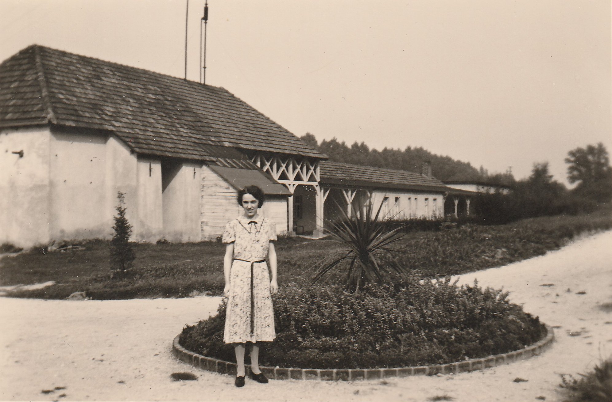 Junge Frau steht vor einer Blumeninsel hinter dem Kohlensäure-Werk St. Josepf in Bodendorf/Ahr (Heimatarchiv Bad Bodendorf CC BY-NC-SA)